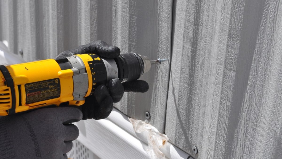 Persona usando un taladro atornillador para fijar tornillos en un panel de madera